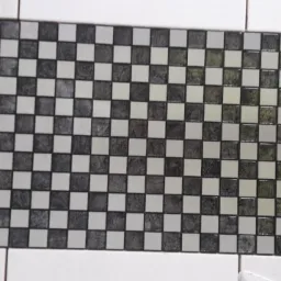 Szachownica z mozaiki ceramicznej w odcieniach szarości i bieli, ułożona jako dekoracyjny pas na ścianie wyłożonej białymi płytkami.