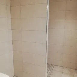 Beżowa kabina prysznicowa typu walk-in z odpływem liniowym w podłodze, widok z boku, neutralne oświetlenie.