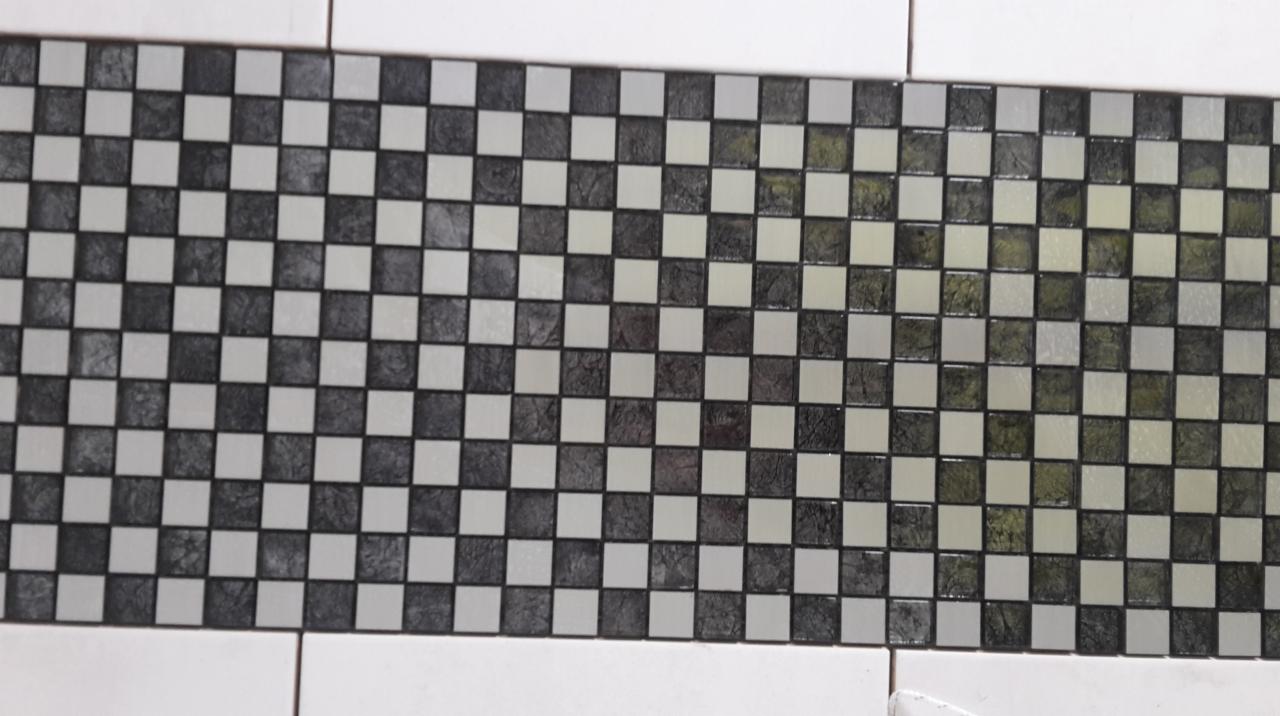 Szachownica z mozaiki ceramicznej w odcieniach szarości i bieli, ułożona jako dekoracyjny pas na ścianie wyłożonej białymi płytkami.