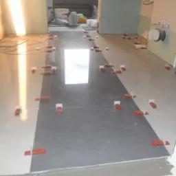 Układanie płytek podłogowych w łazience z użyciem krzyżyków dystansowych, widoczne fragmenty instalacji i przygotowane ściany do wykończenia.