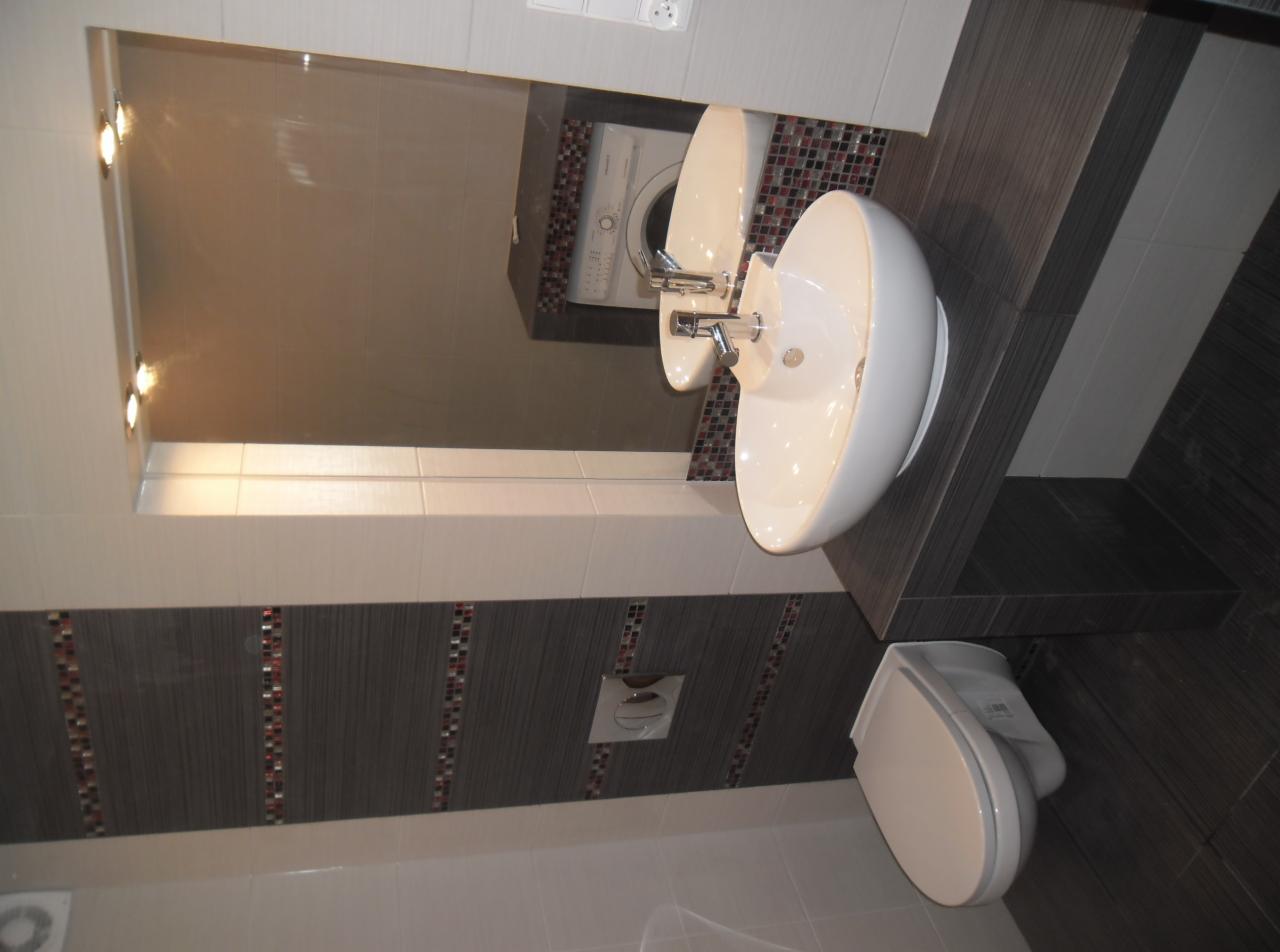 Nowoczesna łazienka po remoncie: biała umywalka nablatowa, toaleta i lustro z oświetleniem. W tle widoczna pralka, ciemne płytki z mozaiką.