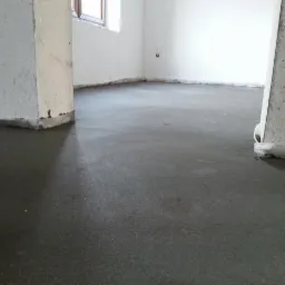 Świeżo wylana, gładka, szara posadzka w surowym wnętrzu z białymi ścianami i oknem w tle.