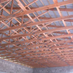 Konstrukcja wiązarów dachowych z widoczną blachą trapezową od spodu, zamocowana do surowych ścian z bloczków betonowych.