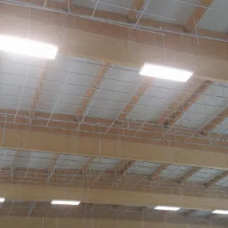 Montaż sufitu podwieszanego z drewnianymi belkami i oświetleniem LED. Metalowa konstrukcja nośna w siatkę. Widok z dołu na konstrukcję sufitu.