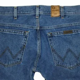 Niebieskie jeansy marki Wrangler, widok z tyłu, z charakterystycznym wzorem na kieszeniach i skórzaną naszywką z logo na pasku.