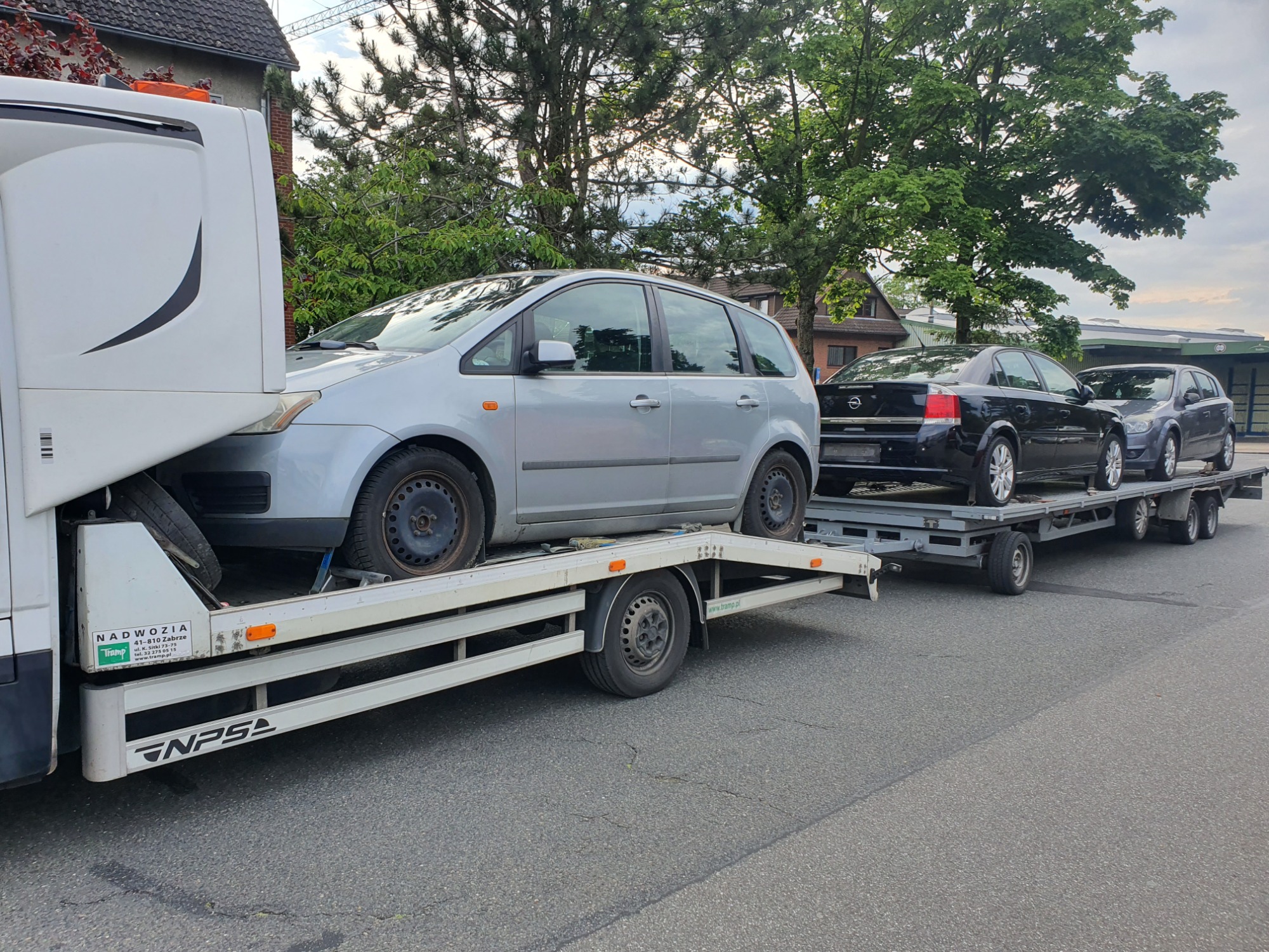 Laweta z trzema samochodami osobowymi na platformie, srebrny Ford C-Max na przodzie, widoczna zabudowa lawety z logo firmy Nadwozia Tramp