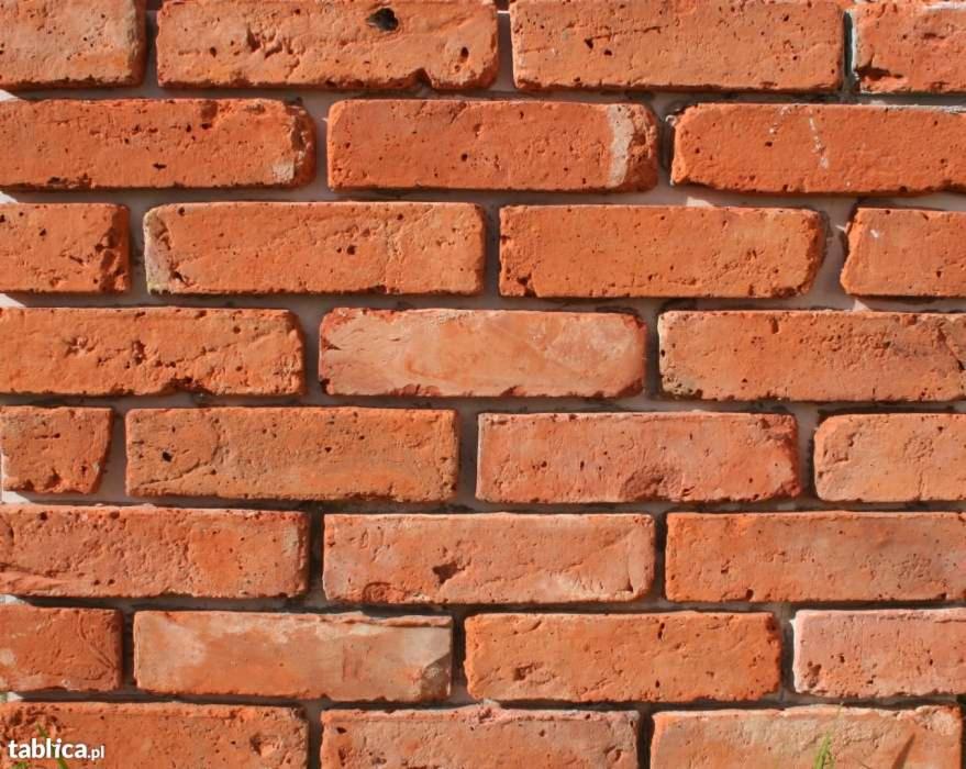 Fragment ściany z czerwonej cegły poniemieckiej, widoczne nierówności i porowata struktura, spoiny między cegłami wypełnione szarą zaprawą.