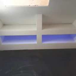 Poddasze po remoncie: białe ściany wyłożone płytkami, podświetlane wnęki z niebieskim oświetleniem LED, ciemna podłoga z płytek, widoczny fragment okna dachowego.