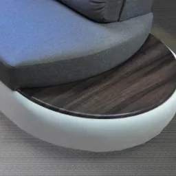 Detal sofy modułowej z drewnianym blatem: szara tapicerka, biała podstawa i blat z ciemnego drewna o wyraźnym usłojeniu. Nowoczesny design.