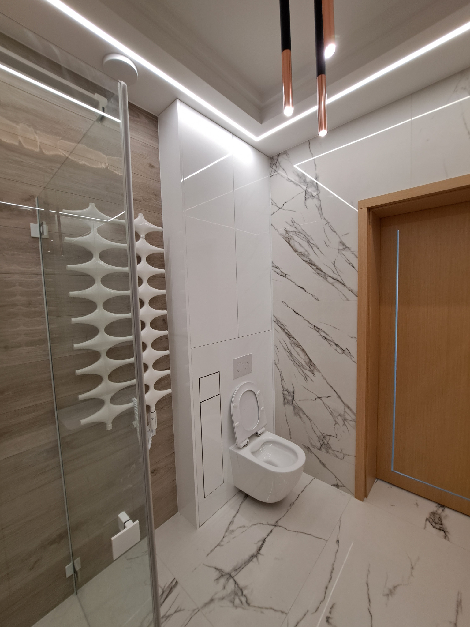 Nowoczesna łazienka z marmurowymi płytkami, podświetleniem LED, grzejnikiem drabinkowym i wiszącą toaletą z otwartą klapą