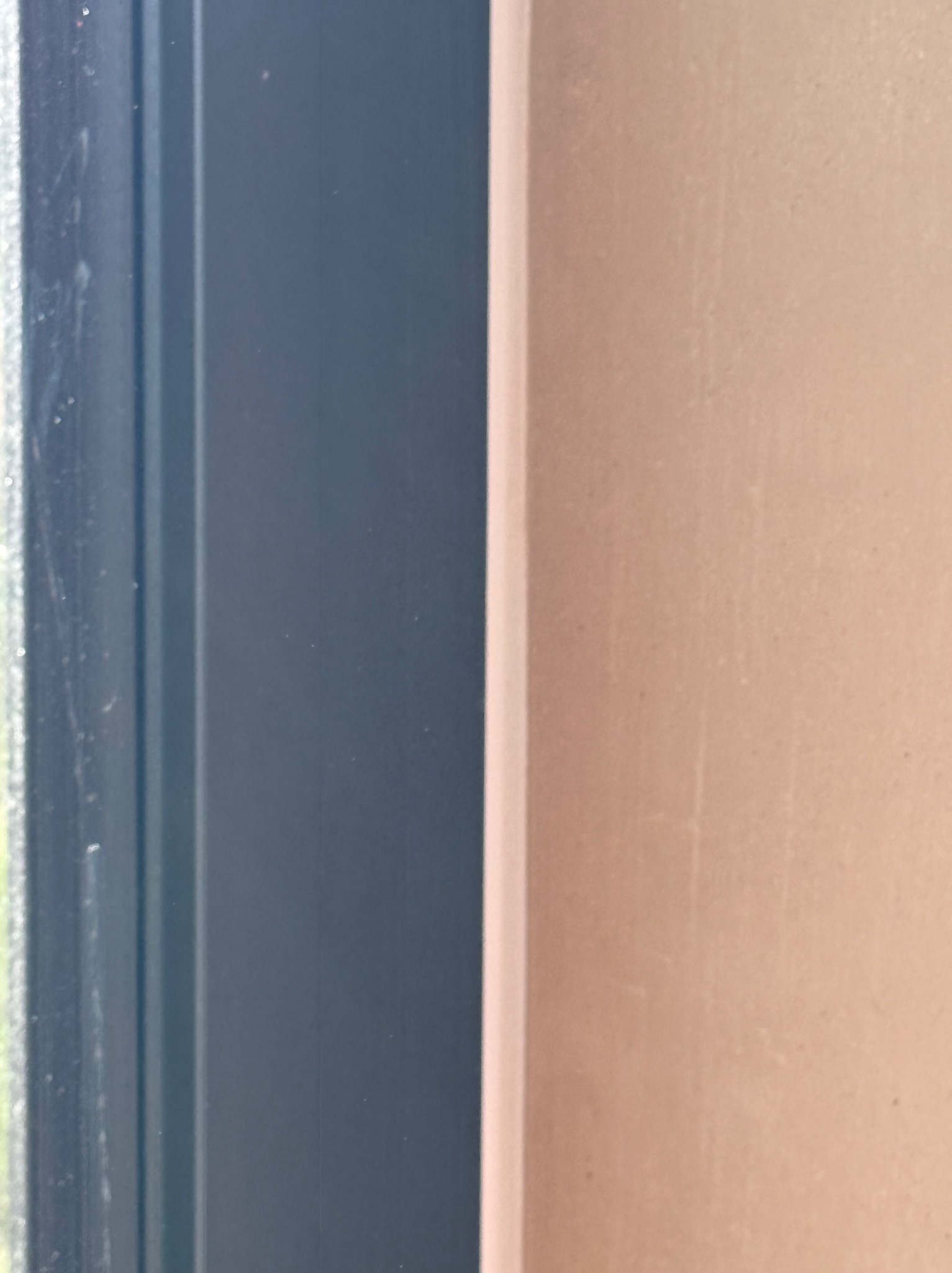 Gładka, jasna ściana po nałożeniu tynku, widoczny fragment okna o ciemnej ramie z delikatnymi smugami.