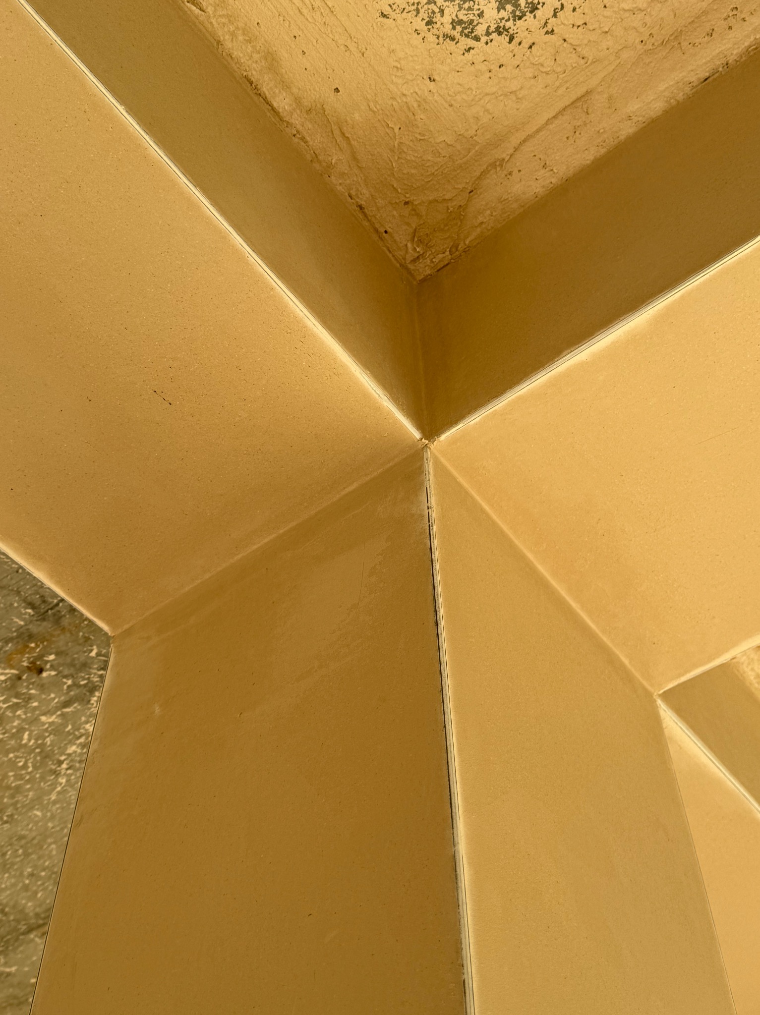 Świeżo nałożony, beżowy tynk maszynowy w rogu pomieszczenia, widoczne niedoskonałości na suficie i łączeniach ścian.