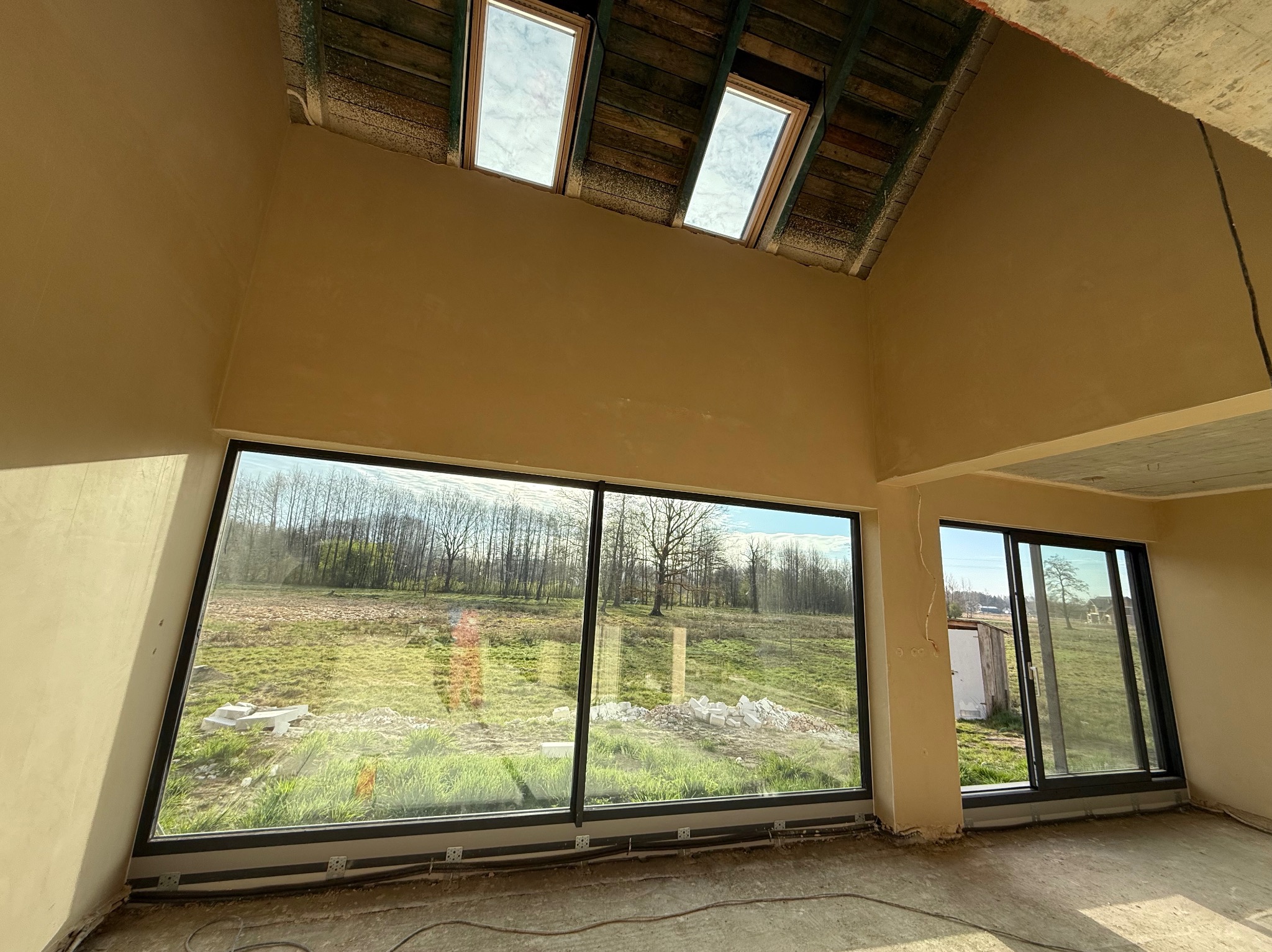 Surowe ściany po nałożeniu gładzi w nowo budowanym domu z dużymi oknami i drewnianym stropem z oknami dachowymi.