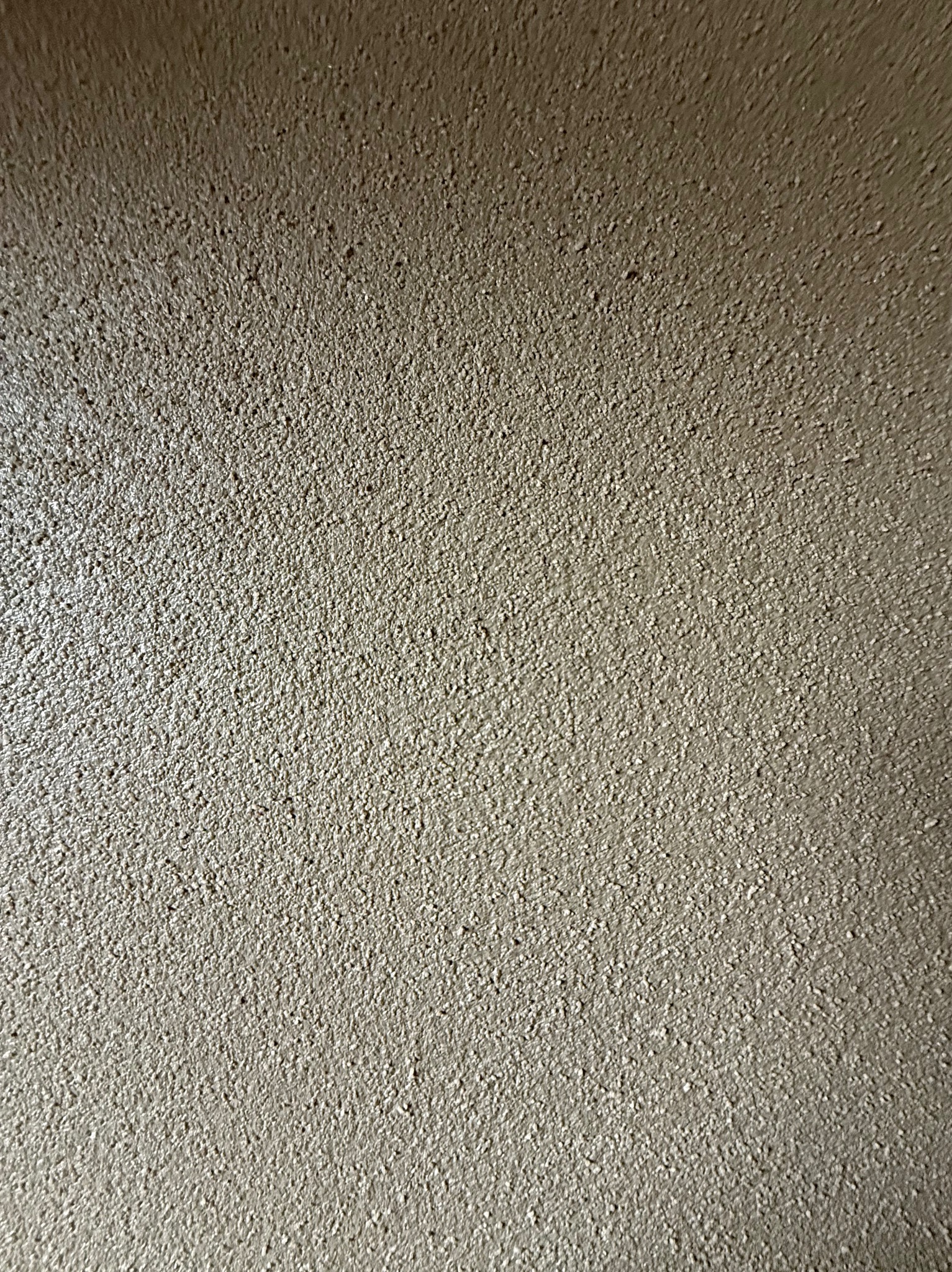 Świeżo nałożony, szary tynk z wyraźną, drobną fakturą, oświetlony z góry, ukazujący nierównomierne rozłożenie materiału.