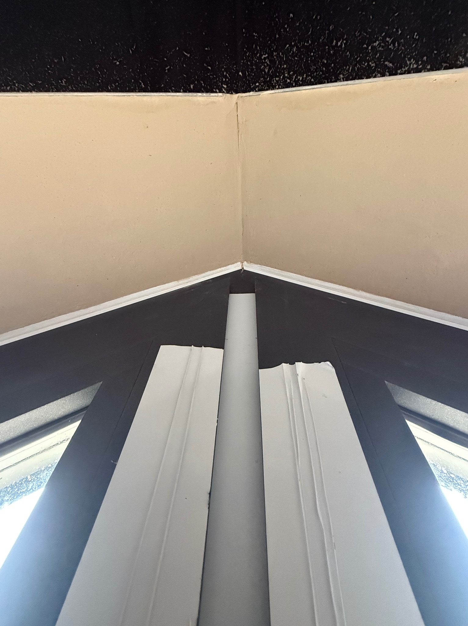 Spojrzenie w górę na gładko wykończony narożnik ściany i sufitu po nałożeniu tynku maszynowego, widoczne ramy okienne w kolorze grafitowym.