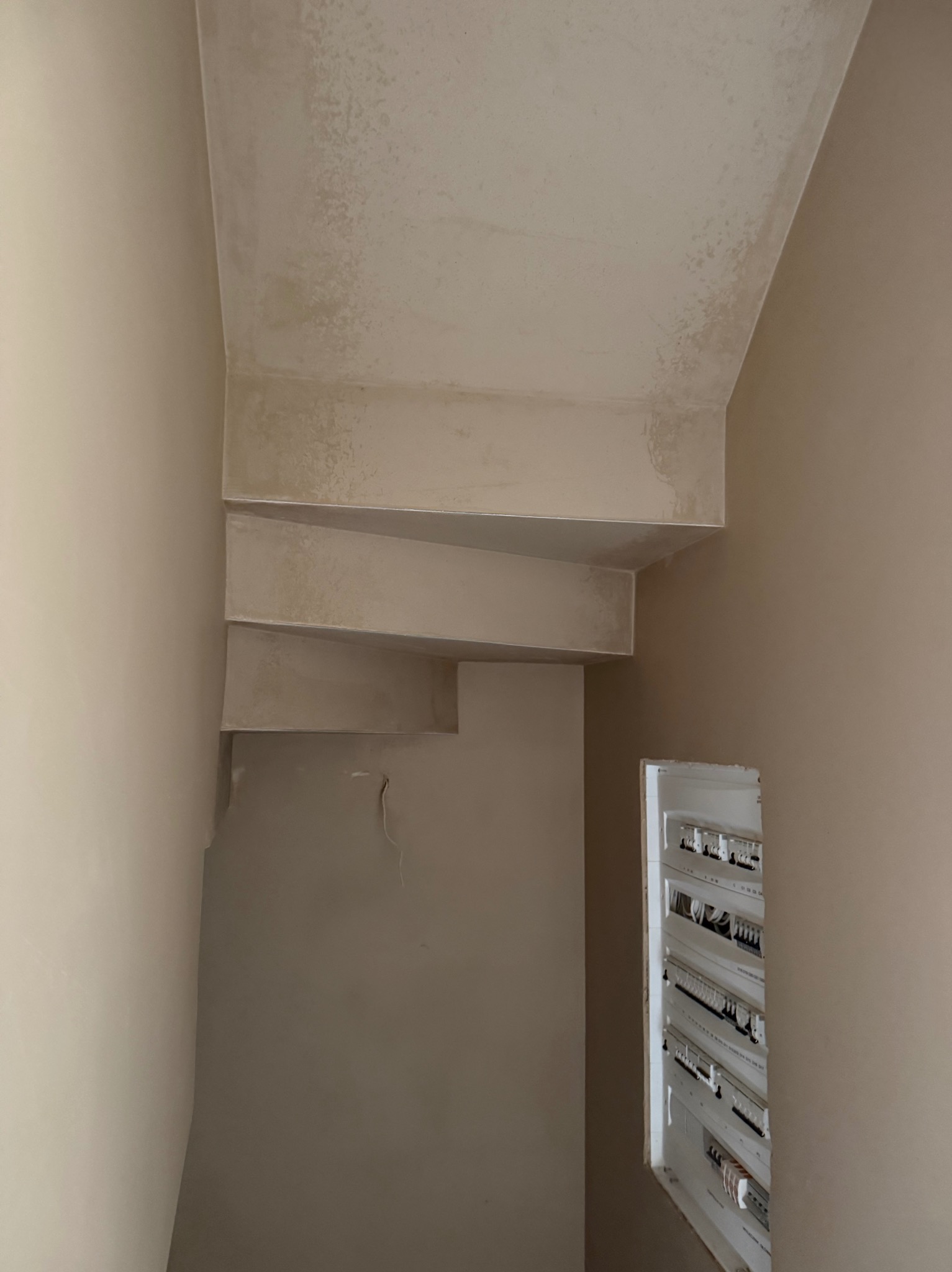 Ściana i sufit po nałożeniu jasnej, gładkiej warstwy tynku. Widoczna skrzynka elektryczna w ścianie.