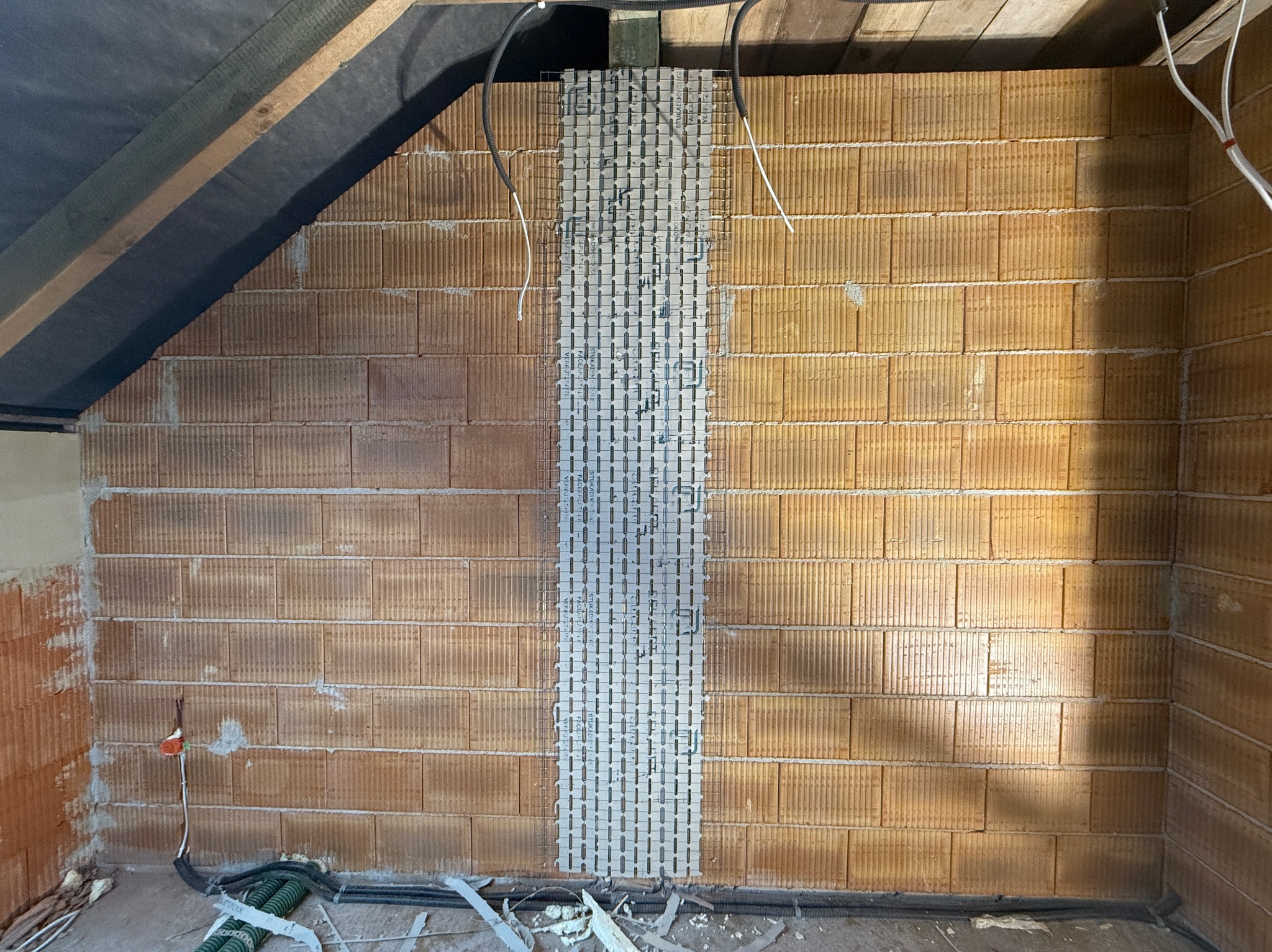 Ściana z pustaków ceramicznych z fragmentem siatki zbrojeniowej, przygotowana do nałożenia tynku maszynowego na poddaszu.