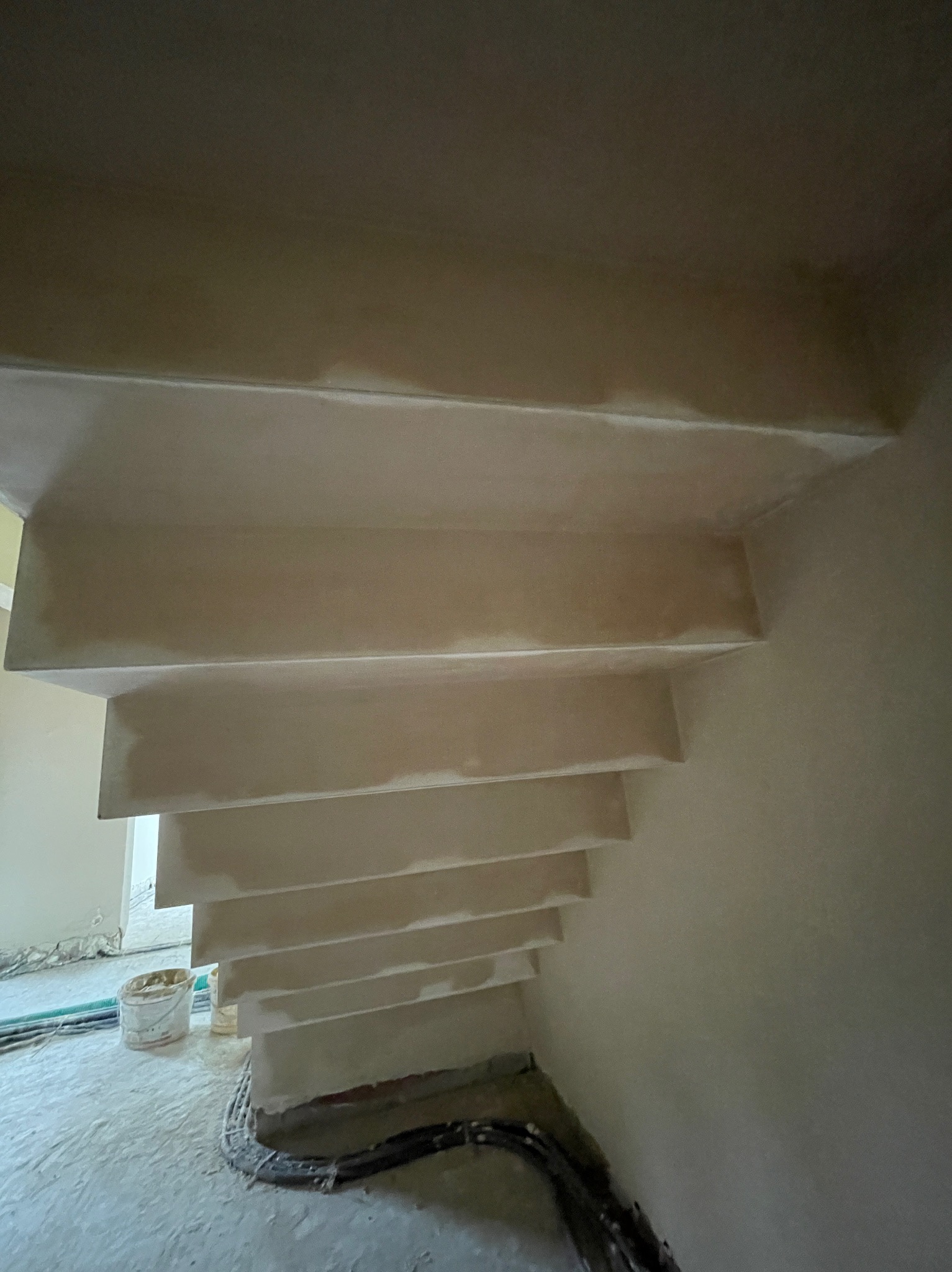 Surowe schody betonowe, przygotowane do dalszych prac wykończeniowych, z widocznymi śladami świeżego tynku i przewodami na podłodze.