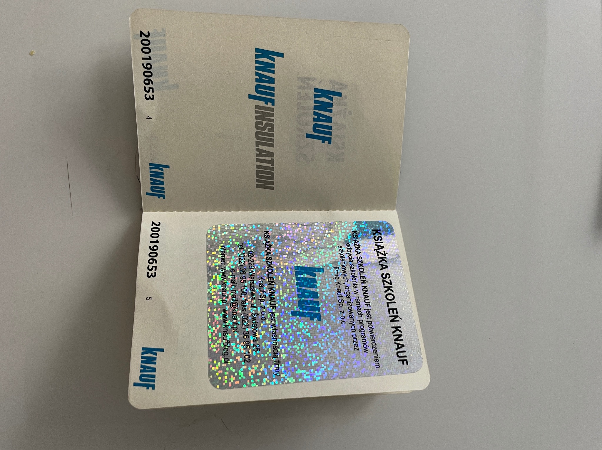 Otwarta książeczka szkoleniowa Knauf z hologramem, prezentująca logo Knauf Insulation i adres firmy Knauf Sp. z o.o. w Warszawie.
