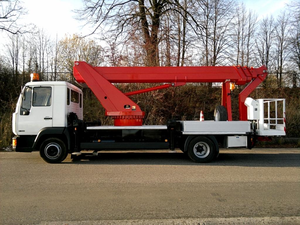 Podnośnik koszowy na samochodzie ciężarowym we Wrocławiu, z czerwoną konstrukcją ramienia i białą kabiną, zaparkowany na asfalcie.