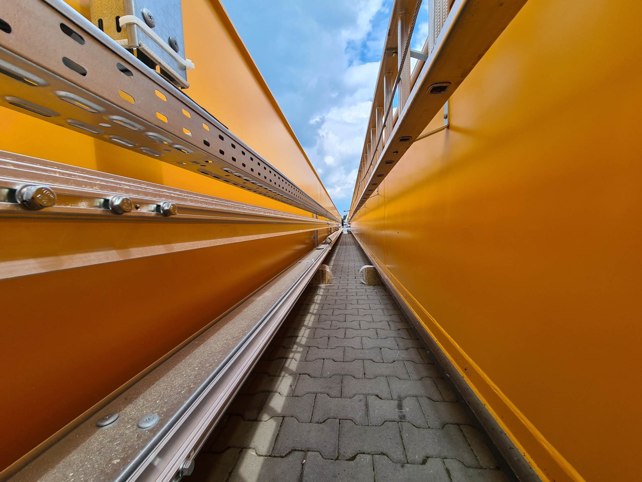 Wnętrze budowanej hali w Kolonowskim z żółtymi ścianami i widoczną konstrukcją stalową oraz drabiną. Nietypowa perspektywa z dołu do góry.