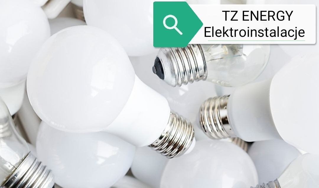 Kompaktowy stos żarówek LED i tradycyjnych z metalowymi gwintami, ułożonych w bliskim planie, z logo firmy elektroinstalacyjnej w rogu.