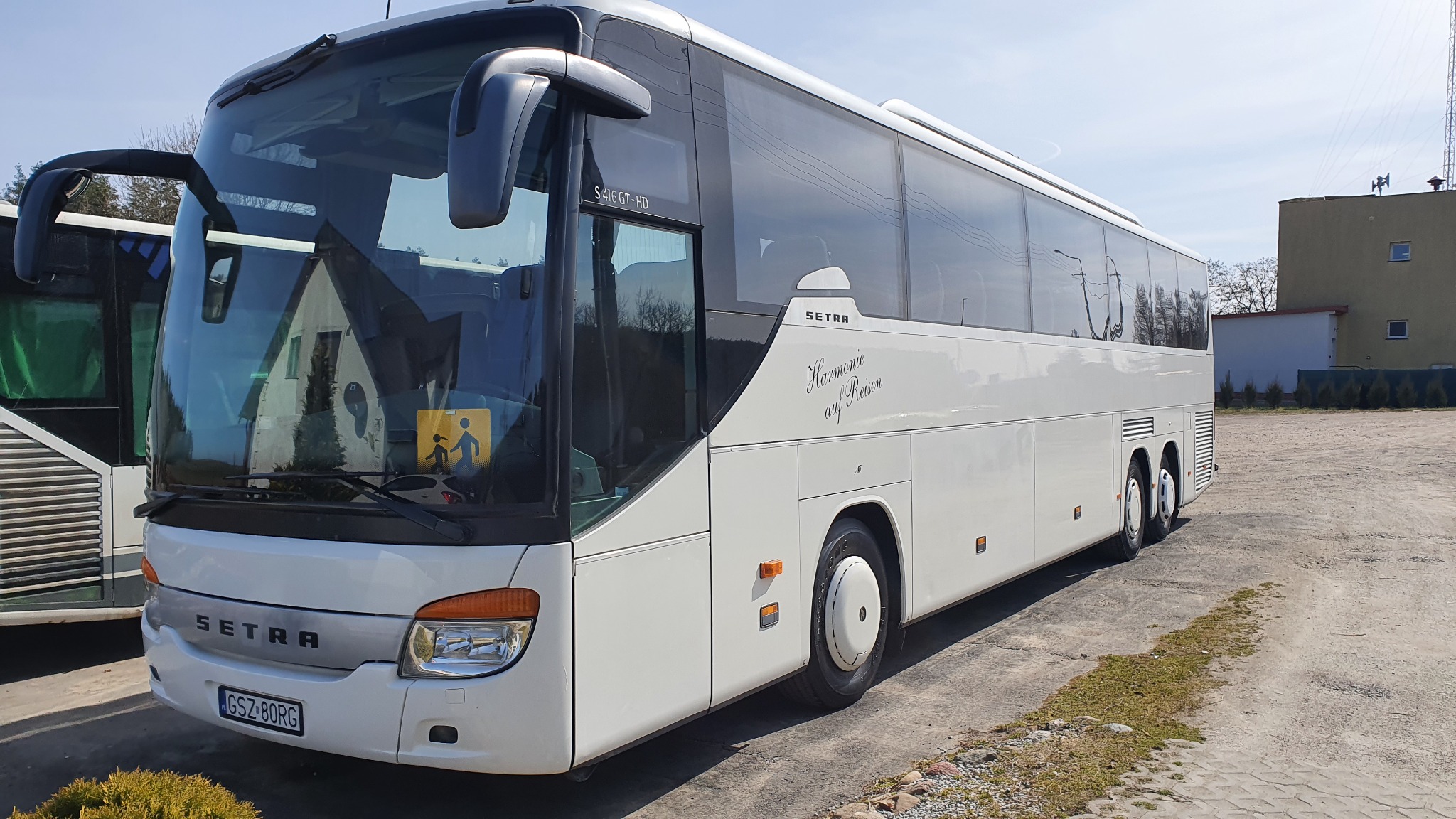 Biały autokar Setra S416 GT-HD z napisem 'Harmonie auf Reisen' na parkingu, widoczny znak ostrzegawczy dla dzieci.