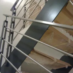 Wnętrze z widokiem na nowoczesne schody z metalową balustradą i drewnianymi stopniami zabezpieczonymi folią, ujęcie z dołu.