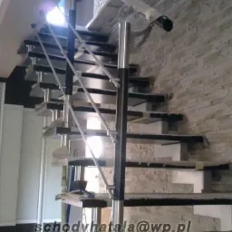 Nowoczesne schody z czarnymi stopniami i balustradą ze stali nierdzewnej, widok z dołu, ściana wykończona kamieniem dekoracyjnym.