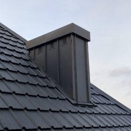 TWÓJ DACH Aleksander Mientki - Ciemnoszary dach z dachówki ceramicznej z obróbkami blacharskimi komina i wentylacji, widok z dołu na tle pochmurnego nieba.