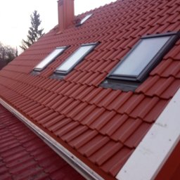TWÓJ DACH Aleksander Mientki - Czerwony dach z dachówki ceramicznej z trzema oknami dachowymi, widok z dołu na fragment rynny i komin w tle.