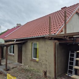 TWÓJ DACH Aleksander Mientki - Dom z nowym, czerwonym dachem z dachówki ceramicznej, widoczne drewniane elementy konstrukcyjne i drabina, elewacja w trakcie wykańczania.