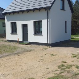 TWÓJ DACH Aleksander Mientki - Nowo wybudowany, jednopiętrowy dom murowany z szarym dachem i czarnymi ramami okiennymi, widoczny z boku, z tymczasowym wejściem na palecie.