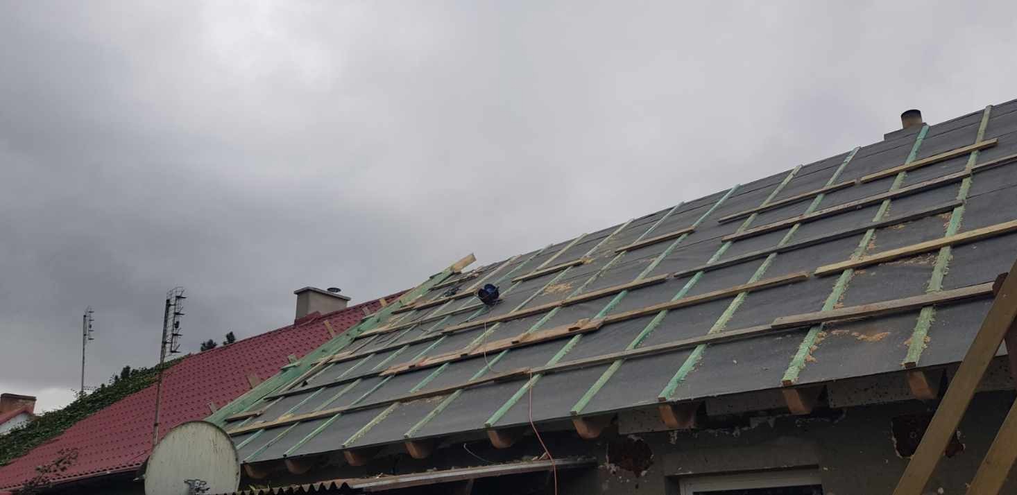 Dach w trakcie układania papy i łat, widoczne przygotowania do położenia nowego pokrycia, pochmurne niebo w tle.