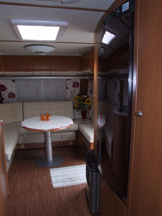 Wnętrze przyczepy kempingowej Fendt Diamant z 2011 roku: jasna tapicerka, okrągły stół z dekoracją, bukiet słoneczników i widoczny grzejnik elektryczny.