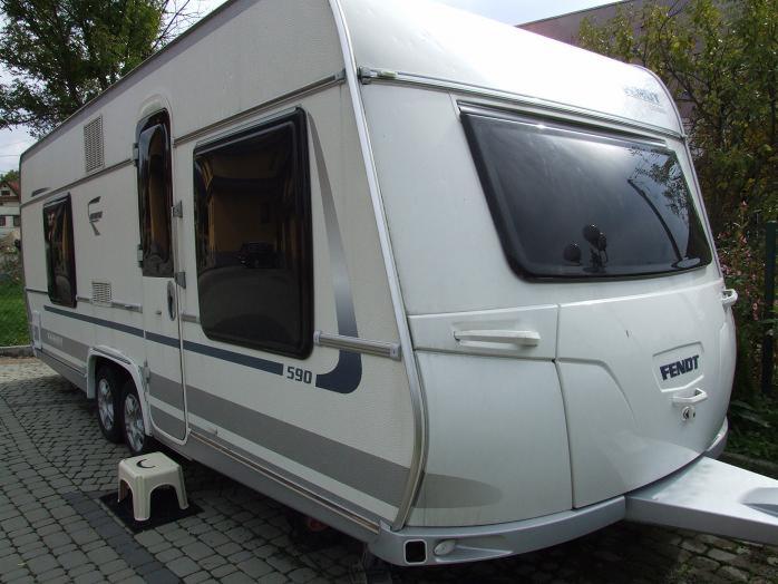 Biała przyczepa kempingowa Fendt Diamant 590 z 2011 roku, zaparkowana na brukowanym podjeździe, widoczny mały plastikowy stołek obok koła.