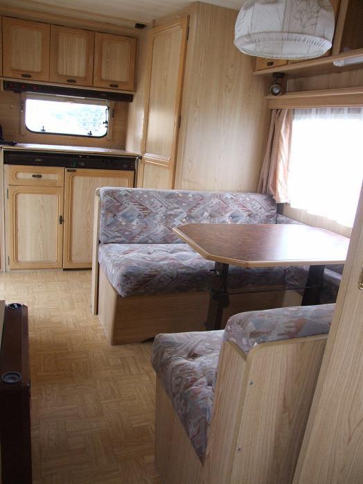 Wnętrze przyczepy kempingowej LMC 490P z drewnianymi meblami, wzorzystą tapicerką i aneksem kuchennym pod oknem.