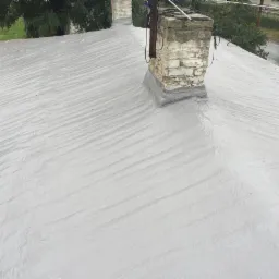 Szarym materiałem pokryty dach z kominem z cegły, widoczny znak drogowy w tle.