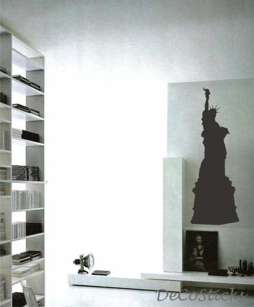 Minimalistyczne wnętrze z naklejką ścienną przedstawiającą Statuę Wolności; obok półka z książkami i dekoracyjny stolik z lampą.