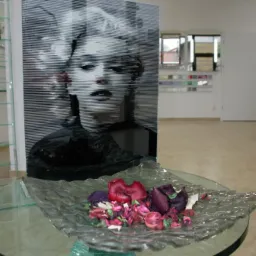 Szklany panel z grafiką Marilyn Monroe na szklanym stoliku z dekoracją kwiatową, w tle okno i próbki kolorów. Unikalny design szkła.