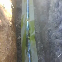 Rura gazowa w żółtej folii ochronnej ułożona w wykopie w ziemi, widoczne ściany wykopu z różnymi warstwami gleby.