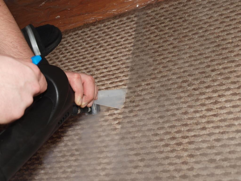 Czyszczenie brązowego dywanu parowym odkurzaczem ekstrakcyjnym, widoczna para i różnica w kolorze po czyszczeniu.