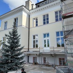 Z.U.H. MATEX-BUD Mateusz Wacławski - Elewacja budynku w trakcie renowacji z widocznymi rusztowaniami i zabezpieczonymi oknami, na pierwszym planie srebrny świerk.