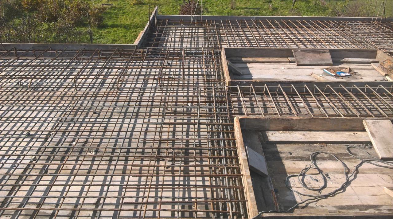 Siatka zbrojeniowa ułożona na deskowaniu szalunkowym, przygotowana do zalania betonem, widok z góry na plac budowy.