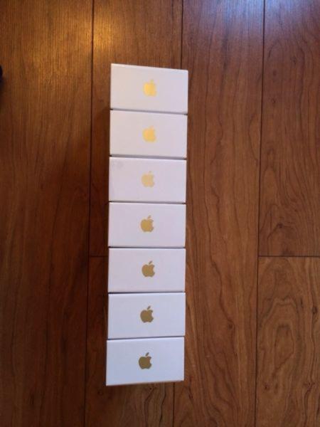 Siedem białych pudełek iPhone 5s z logo Apple ułożonych pionowo na drewnianej podłodze.