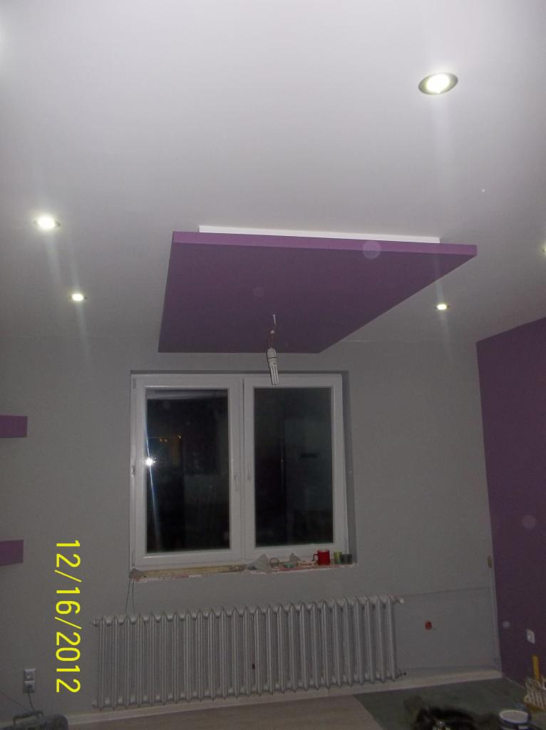 Pokój po odświeżeniu: szare ściany, fioletowy akcent na suficie z oświetleniem punktowym i grzejnikiem pod oknem. Widoczny fragment ściany pomalowany na fioletowo.