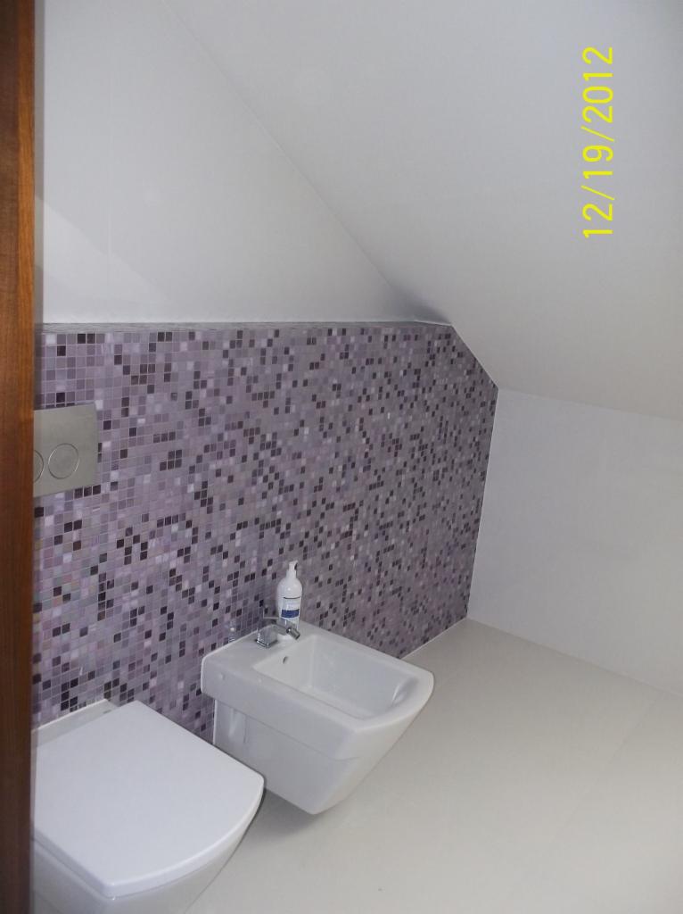 Biała toaleta i bidet w łazience na poddaszu, ściana wyłożona mozaiką w odcieniach fioletu i szarości, widoczny dozownik mydła. Ukończony remont łazienki.