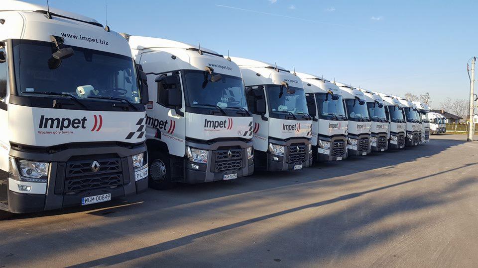 Flota białych ciężarówek marki Renault z logo firmy Impet zaparkowana w rzędzie na parkingu w słoneczny dzień.