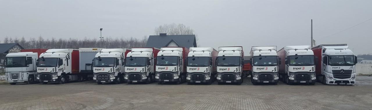 Flota białych ciężarówek z logo firmy transportowej zaparkowana na placu, widok z przodu, pochmurny dzień.
