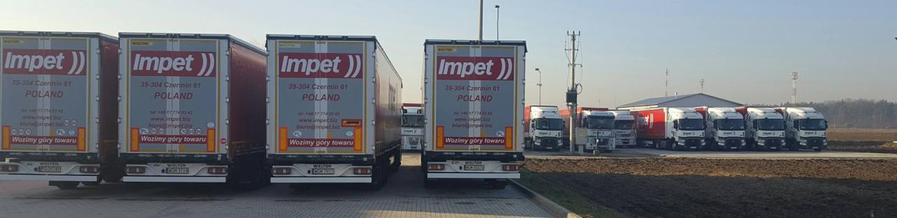 Flota ciężarówek firmy Impet zaparkowana na placu, widoczne naczepy z logo firmy i dane kontaktowe, w tle budynek magazynowy.